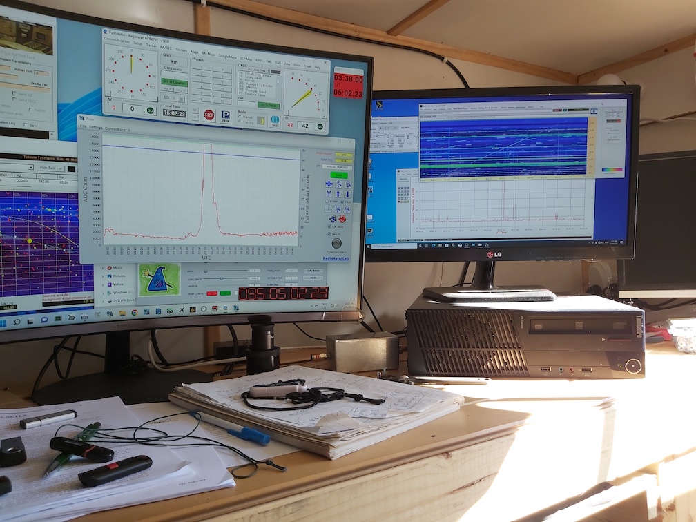 A photo of two computer monitors on a wooden desk displaying Radio JOVE data.
