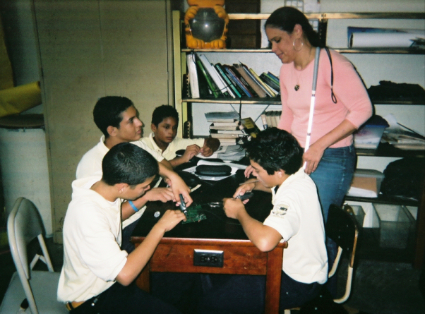 Four students working on building an RJ kit with Wanda Diaz advising them on the soldering technique.
