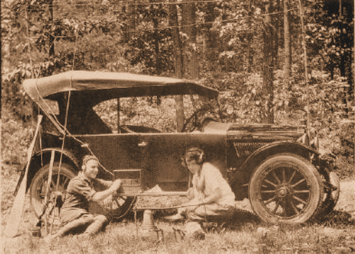 An old photo of two people listening to the radio in front of their car